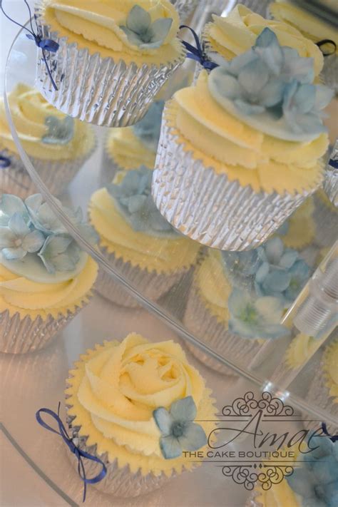 Cupcakes With Yellow Frosting And Blue Flowers Are On A Clear Platter