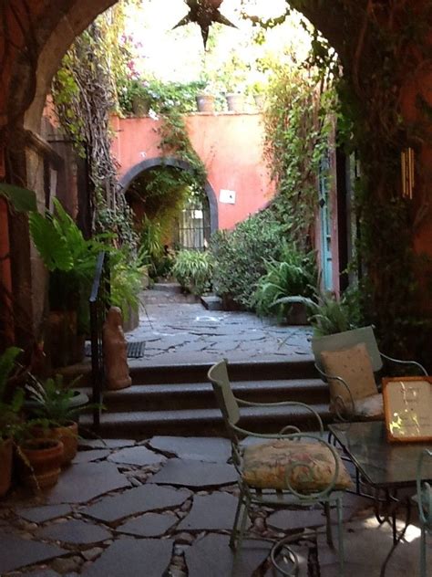 An Archway Leading To A Patio With Tables And Chairs On It Surrounded