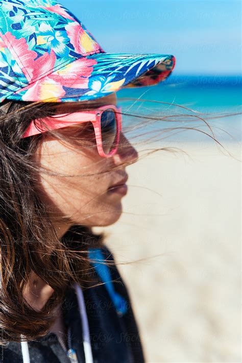 Stylish Young Woman Wearing Pink Sunglasses And A Colourful Cap On A Windy Day In The Beach