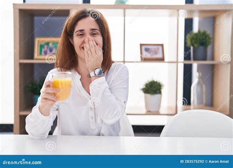 Brunette Woman Drinking Glass Of Orange Juice Laughing And Embarrassed