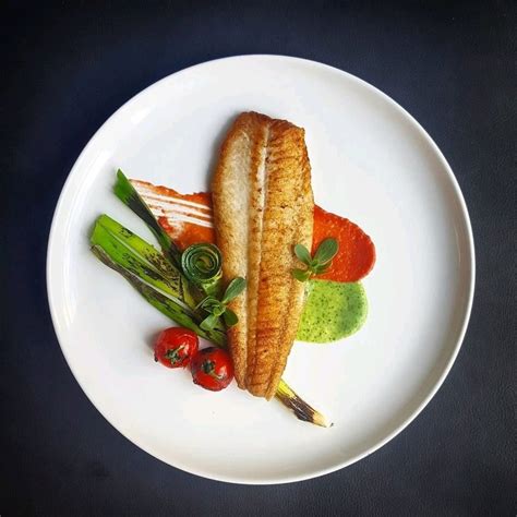 A White Plate Topped With Fish And Veggies On Top Of A Black Table