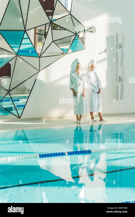 Attractive Young Women In Bathrobes Standing Next To Swimming Pool At