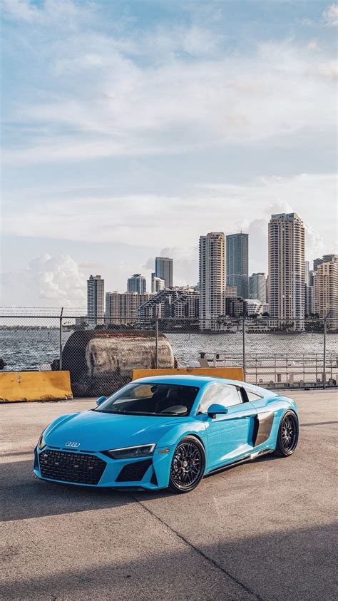 a blue sports car parked in front of the ocean with a city skyline ...