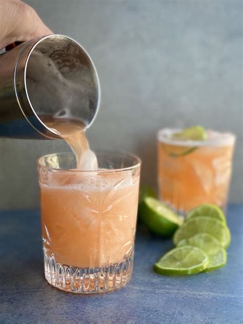 A Person Pours A Drink From A Pitcher Into A Glass With Lime Slices On