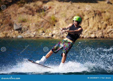 A Young Man Wearing A Helmut And Lifejacket Wakeboarding On A Lake A