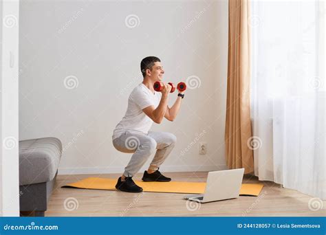 Indoor Shot Of Sporty Athletic Man Wearing Sportswear Doing Sport Exercises At Home Squatting