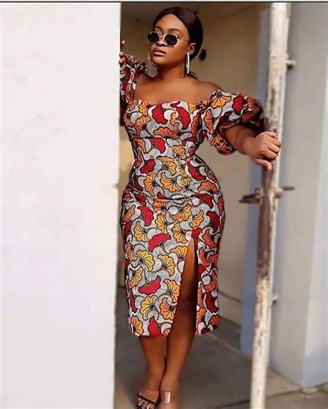 A Woman In An African Print Dress Is Leaning Against A Wall And Posing