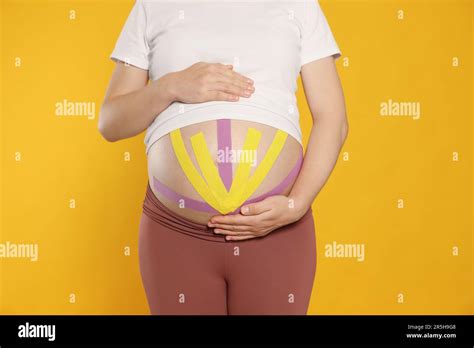 Pregnant Woman With Kinesio Tapes On Her Belly Against Orange