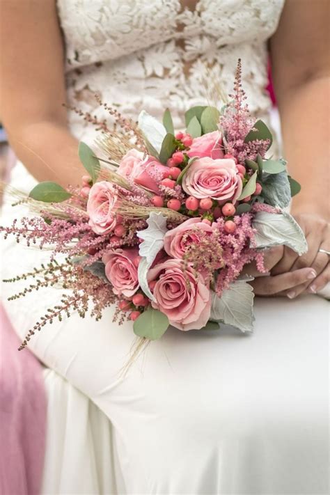 A Bride Holding A Bouquet Of Pink Roses And Greenery In Her Hand While