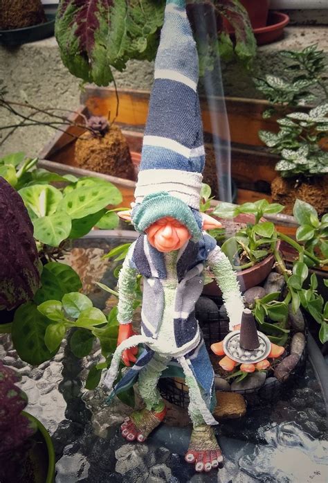 A Gnome Figurine Sitting On Top Of A Table Next To Potted Plants