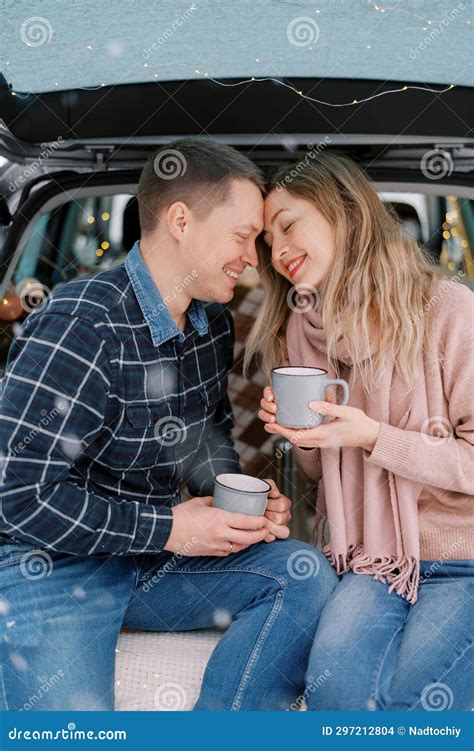 Smiling Man And Woman Touching Foreheads While Sitting With Cups In Car