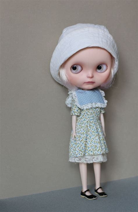 A Doll With White Hair Wearing A Blue Dress And Black Shoes Is Standing