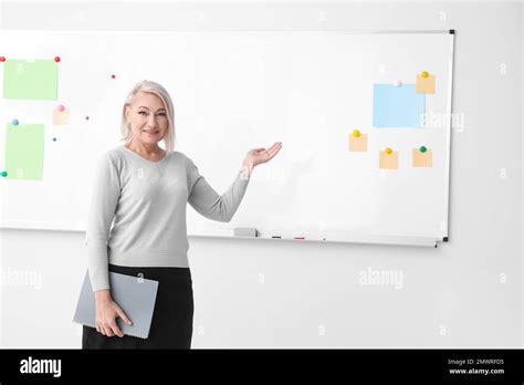 Mature Teacher With Notebook Near Whiteboard In Classroom Space For