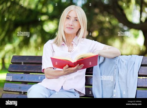 Portrait Of Serene Mature Woman Reading Book In The Summer Park Stock