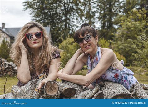 Ritratto Di Due Donne Mature E Amichevoli In Vacanza Posate Su Una Pila Di Legno Fotografia