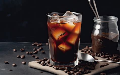 Un vaso de café con hielo en una mesa junto a una cafetera y granos de