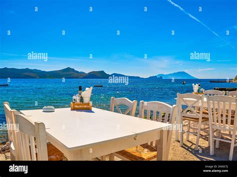 White Chairs And Tables Of Greek Tavern By Waterfront At Day Vacations