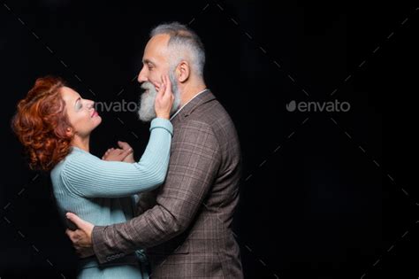 Beautiful Mature Couple Standing Embracing And Looking At Each Other Isolated On Black Stock