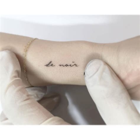 "De noir" lettering tattoo handwritten on the wrist.