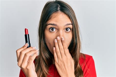 Young Brunette Woman Holding Red Lipstick Covering Mouth With Hand