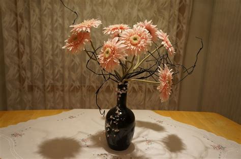 A Black Vase Filled With Pink Flowers On Top Of A Wooden Table Covered