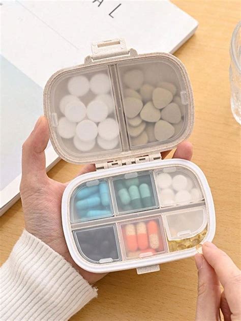 A Person Holding An Open Pill Box On Top Of A Wooden Table Next To A Glass