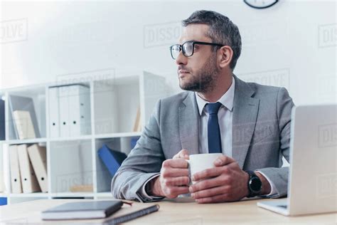 Serious Businessman In Eyeglasses Holding Cup Of Coffee And Looking