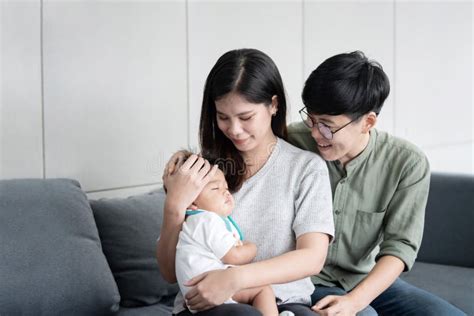 Asian Lesbian Couple Holding Their Sleep Adopted Baby In Their Arms On The Sofa Stock Photo
