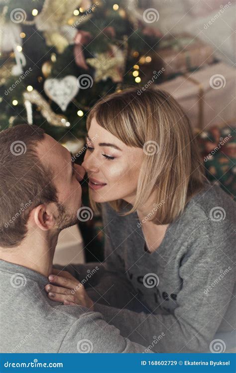 Loving Young Couple Spends Christmas At Home Near A Decorated Festive Christmas Tree Man And