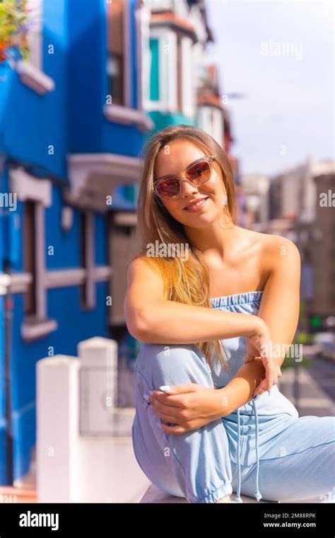 Portrait Of Attractive Young Blonde Woman Wearing Sunglasses Behind Blue Colorful Facade Stock