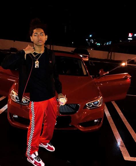 A Man Standing Next To A Red Car In A Parking Lot With His Hand On His Hip