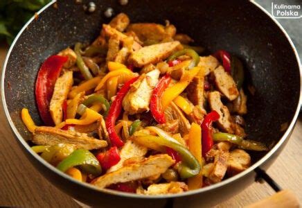 A Wok Filled With Chicken And Peppers On Top Of A Wooden Table