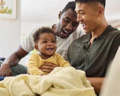 Same Sex Male Couple Or Friends Playing With Baby Sitting On Sofa At Home Together Stock Image