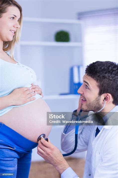 Smiling Doctor Examining Stomach Of Standing Pregnant Patient Stock