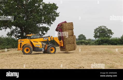 Man Using A Telehandler To Load Bales Of Straw Onto A Tractor Trailer