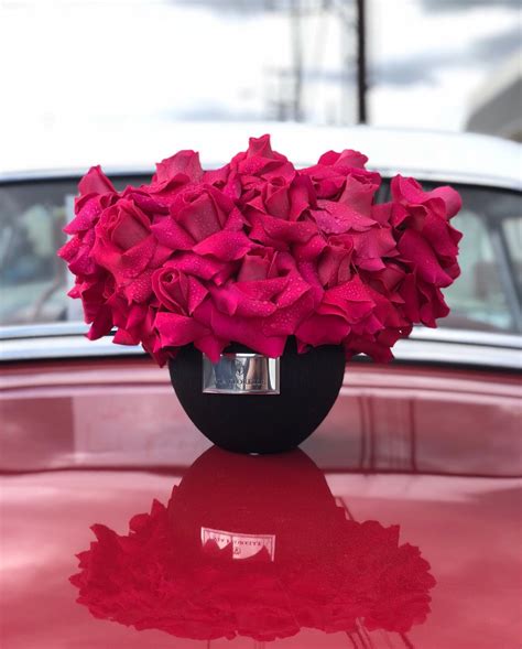 A Vase Filled With Pink Flowers Sitting On Top Of A Red Car S Hood