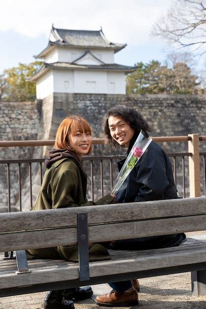 Pareja Japonesa Posando Sentada En Un Banco Al Aire Libre Foto Gratis