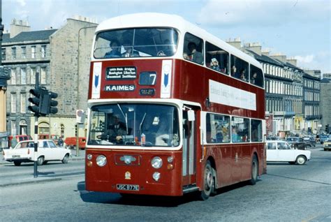 a red double decker bus driving down a street next to tall buildings ...