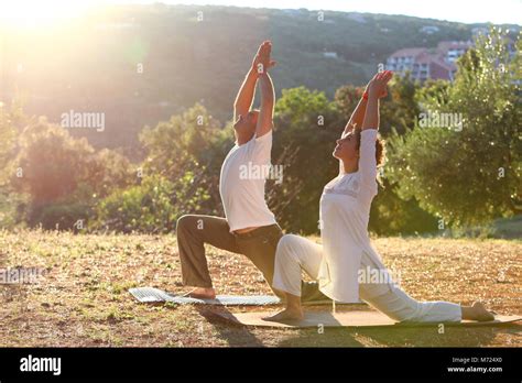 Young Couple Practice Yoga Outside In Nature During Sunrise On Their