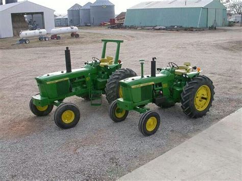 Two Green Tractors Are Parked On The Gravel