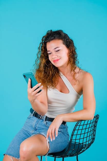 Free Photo Smiling Girl Is Looking At Her Phone Screen On Blue Background