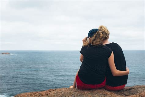 Back View Of Two Teen Girls Sitting On A Rock Looking Out On The