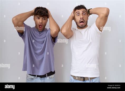 Homosexual Gay Couple Standing Over White Background Crazy And Scared With Hands On Head Afraid