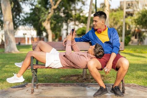 Hombre acostado en un banco mientras mira el teléfono móvil con su pareja gay Foto Premium