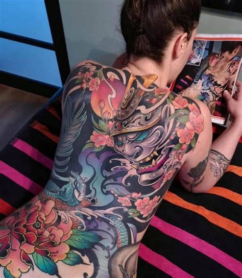 A Woman With Tattoos On Her Back Is Laying Down And Looking At A Photo