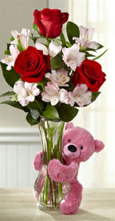 A Pink Teddy Bear Sitting Next To A Vase Filled With Red Roses And White Lilies