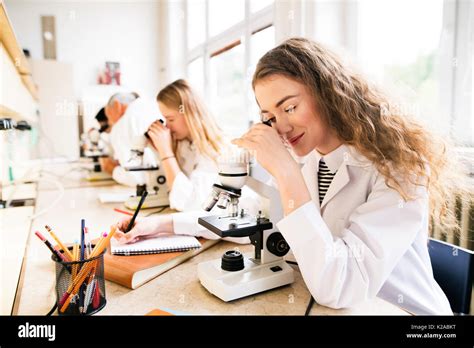 Beautiful High School Students With Microscopes In Laboratory Stock