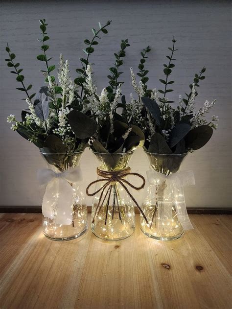 Two Vases With Flowers And Greenery Are Sitting On A Wooden Table