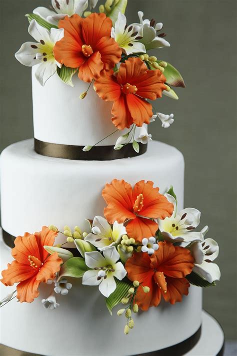 A Three Tiered White Cake With Orange Flowers On Top