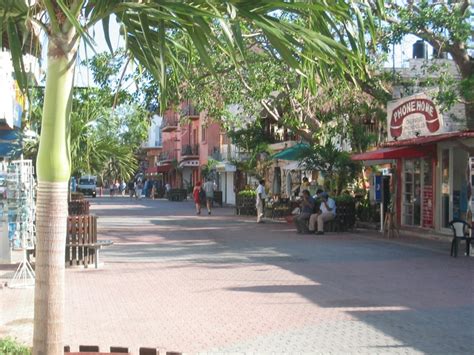 People Are Sitting On Benches In The Middle Of A Street With Shops And